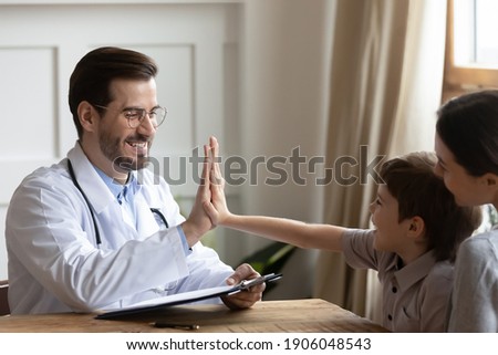 Happy young Caucasian male doctor give high five to cute small 7s boy patient at consultation with mom in hospital. Smiling pediatrician make deal cheer little kid child in clinic. Healthcare concept.