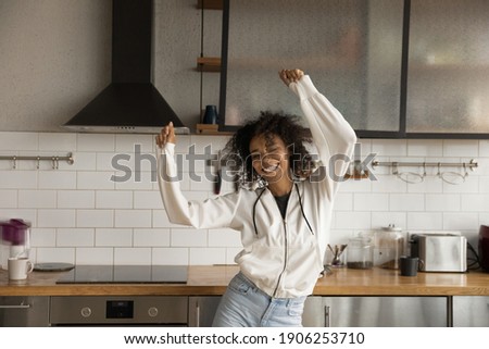 Going crazy. Funny positive young african female dancing at modern kitchen in good mood laughing having fun alone. Joyful millennial black female relaxing on weekend moving in dance by active music