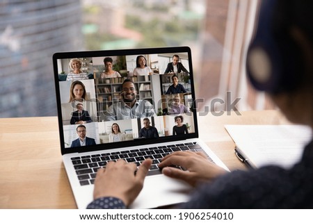 Over shoulder view of female in headset take part in distant virtual briefing video conference using laptop. Young woman employee meet with diverse colleagues online discuss work affairs on quarantine