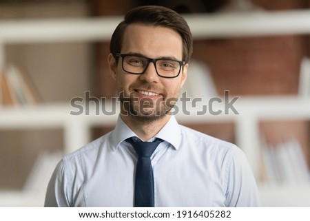 Headshot portrait of smiling young Caucasian businessman in suit and glasses pose in office. Profile picture of happy successful male director or CEO show leadership and optimism. Success concept.