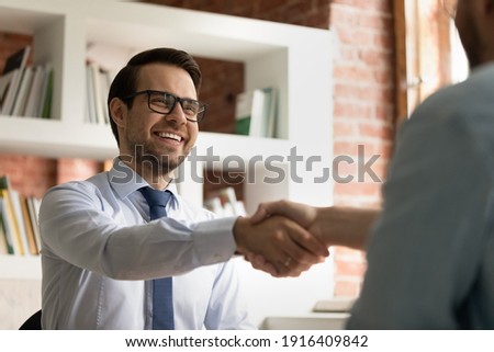 Smiling young Caucasian businessman shake hand of partner or colleague close deal after successful meeting in office. Happy male CEO or employee handshake get acquainted greet with business client.
