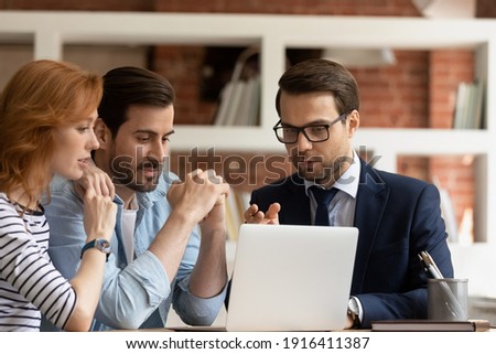 Caucasian male real estate agent or broker consult couple clients show project on laptop screen. Man realtor or financial advisor talk have consultation with spouses at office meeting. Rental concept.