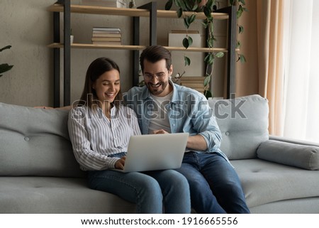 Happy husband wife newlyweds rest on sofa hold laptop choose furniture for new home buy consumer goods online. Young family couple using pc discuss flat renovation options planning trip on vacation