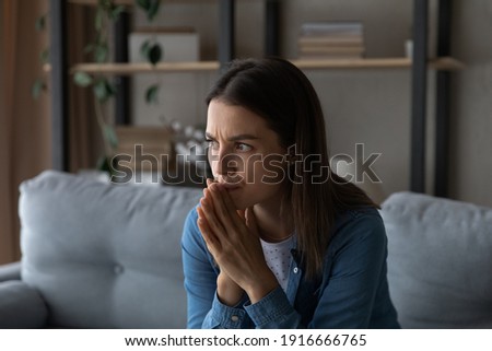 Worried young woman sit on sofa look aside lean forward with folded hands feel fear anxiety. Teen female stressed with unwanted pregnancy thinking on abortion hesitate have doubts making hard decision