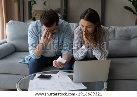 Confused upset millennial married couple sit on couch read financial papers invoices troubled with too high expenses utility costs. Worried young spouses deal with debt bankruptcy of family business