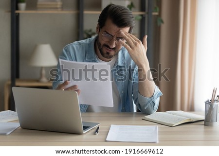 Confused shocked self employed businessman holding paper letter informing about accumulated bank debt unexpected financial problem. Upset stressed young male enterpreneur get loan application rejected