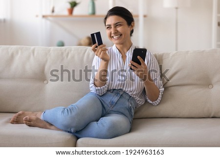 Excited indian female bank customer use phone to make easy secure payments online in convenient app. Glad mixed race lady dream of spending bonus cashback received on credit card for internet paying