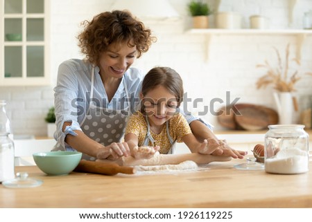 In four hands. Loving family of single mother small daughter child baking cake pastries cooking pie on dessert. Happy young mom bake sweet cookies with little kid roll dough at kitchen table using pin