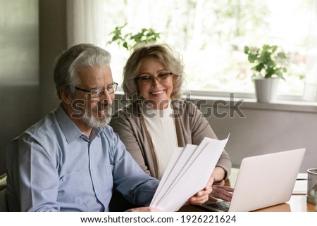 Excited elder family pensioner couple read and check financial document, calculate profit, saving income from investment. OAP Senior man and 50s woman do monthly paperwork, make utility payment online