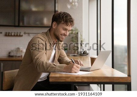 Close up smiling young man using laptop, writing, taking notes, watching webinar, training, involved in internet lesson, motivated positive student studying online at home, looking at laptop screen