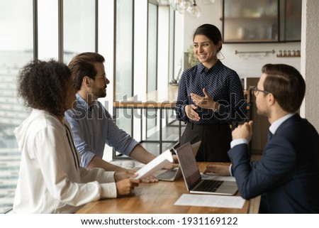 Smiling Indian businesswoman leading corporate meeting with diverse colleagues, coach mentor training employees, discussing project strategy, sharing ideas, business partners negotiation concept