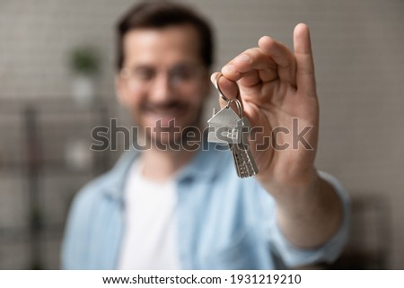 Satisfied homeowner. Blurred portrait of happy young man buyer renter of new modern home apartment holding key demonstrating wellbeing wealth celebrate achievement. Focus on hand with keys of dwelling Stockfoto © 