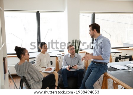 Interested happy young multiracial colleagues sitting on chairs, listening to male boss team leader, explaining working issues at briefing meeting in modern office, international company collaboration Foto stock © 
