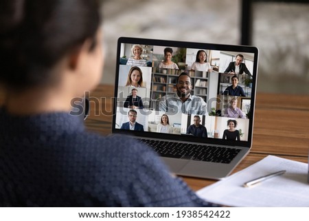 Over shoulder view of female worker have webcam digital virtual conference with diverse multiethnic colleagues. Woman speak talk on video call with multiracial businesspeople. Online meeting concept.