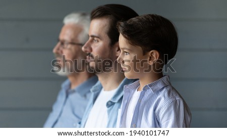 Close up side view of three generations of Caucasian men stand in row look in distance show unity and family support. Small boy with young father and older grandfather reunited. Offspring concept.