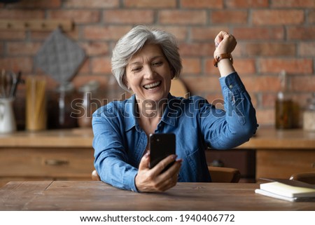 Overjoyed aged senior latin grandmother pensioner yell yes super celebrate winning mobile phone game. Happy elderly female sit at kitchen table read email excited with great sale discount at web shop