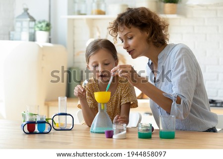Excited young Caucasian mother and little 9s daughter have fun play with chemistry lab game together. Caring playful mom and small teen girl child engaged in interesting scientific activity at home. 商業照片 © 