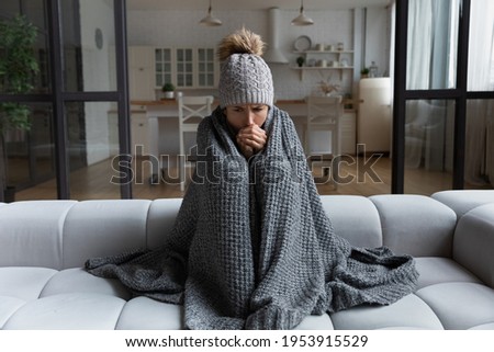 Frozen. Sad latina female sit on couch at freezing cooled studio flat in warm cap and blanket shiver tremble with cold. Unhappy young lady spend time at home feel bad suffer of heating system problems Stock foto © 
