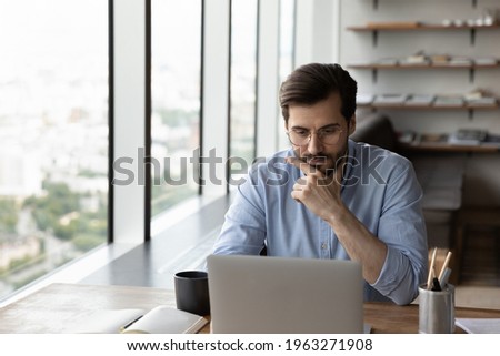 Thoughtful young male employee or worker sit at desk in office work online on laptop solve business problem. Pensive businessman use computer thinking pondering over project. Planning concept. Foto stock © 