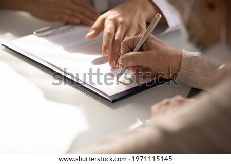 Commercial medicine. Close up of aged woman patient hand signing medical insurance contract at doctor office. Female medic show retired lady client place to put signature on healthcare coverage policy 商業照片 © 
