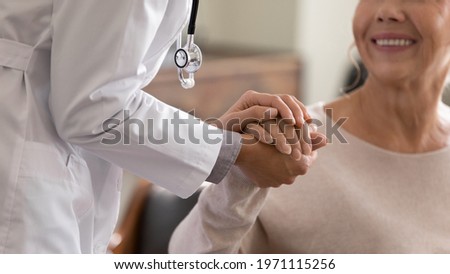 Doctor giving hope. Close up shot of young female physician leaning forward to smiling elderly lady patient holding her hand in palms. Woman caretaker in white coat supporting encouraging old person 商業照片 © 