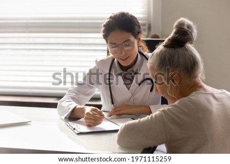 Consulting patient. Capable young latin woman doc counsel female retiree prescribe treatment explain therapy details. Old lady sign informed consent on surgical procedure at attending physician office Photo stock © 
