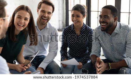 Coach or group leader telling funny story or joke to laughing diverse team. Happy multiethnic employees having fun while discussing project, sharing ideas, informal brainstorming sitting on chairs