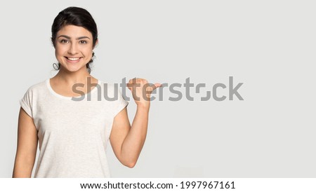 Portrait of smiling Indian woman isolated on grey studio background point at blank empty copy space. Happy millennial mixed race female show good promotion deal or sale discount. Commerce concept.