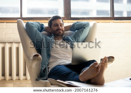 Serene millennial 30s man accomplish work on laptop put hands behind head relaxing on cozy leather armchair at home. Stress-free leisure, fresh conditioned air inside, fatigue relief, day nap concept 商業照片 © 