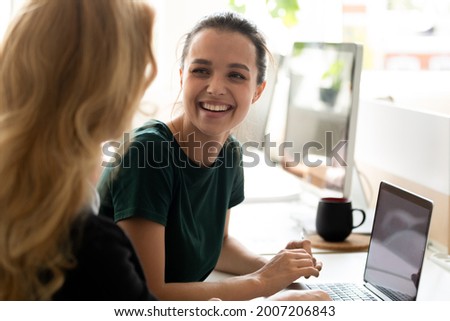 Happy millennial intern, student girl talking to teacher, consulting tutor, mentor at computer in training center, discussing new professional skills, smiling, laughing. Business education, internship