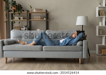 Side view woman enjoy day nap on comfy sofa. Young caucasian female put hands behind hear lying on cushion on cozy couch breath fresh conditioned air inside modern living room. Leisure, repose concept Foto d'archivio © 