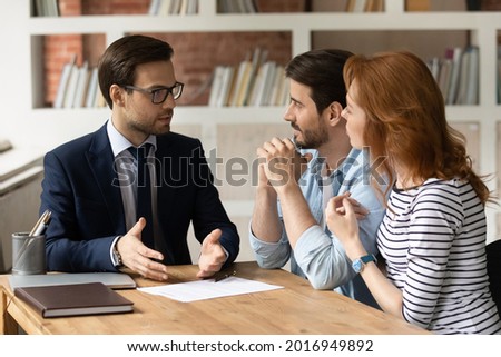 Professional male lawyer financial advisor consulting happy family couple clients in modern office. Interested young customers meeting realtor broker bank worker, discussing agreement or deal.
