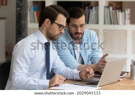 Two serious, confident male office colleagues review collaborative corporate task, discussing on-line business common project using computer. Teamwork, mentoring, partnership, commercial offer concept Foto stock © 
