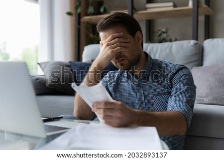 Frustrated desperate millennial man checking bills for payments, holding receipts, getting upset about overspending, too high mortgage, insurance fees. Homeowner analyzing costs, expenses, budget Foto stock © 