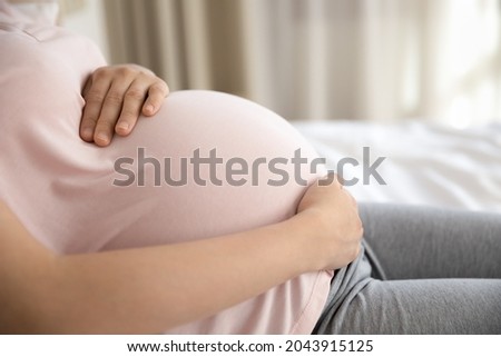 Future mom resting. Cropped shot of tired expectant mom lying in bed stroking baby bump. Young pregnant woman in ninth month take care of health relax alone embrace big belly relieve stress. Close up