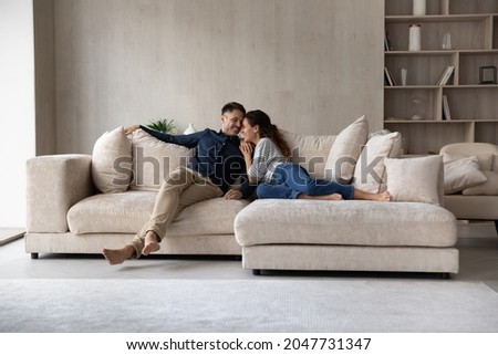 Full length happy relaxed young family couple homeowners or renters lying on big cozy sofa, enjoying carefree leisure weekend time, celebrating moving into new contemporary apartment, tenancy concept. Stockfoto © 