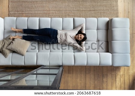 Happy satisfied lazy Asian woman relaxing on big comfortable couch, enjoying comfort, leisure on weekend, sleeping, napping, breathing fresh conditioned air in living room. Top view, full length Foto stock © 
