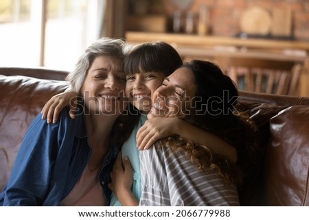 Three female generations family portrait. Cute girl hugging tightly beloved mom and grandma. Mother and grandmother embracing, cuddling granddaughter on couch at home, enjoying leisure time together Stok fotoğraf © 