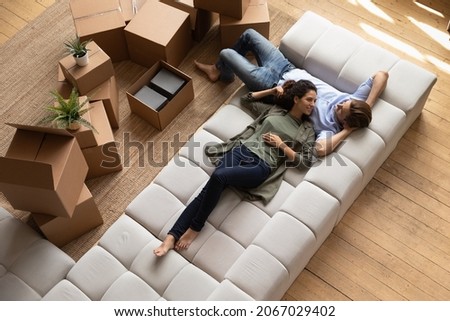 Overhead view peaceful young couple relaxing on fashionable cozy sofa near heap of packed belongings in cardboard boxes, resting at own house at relocation day. Bank loan and mortgage, tenancy concept Stockfoto © 