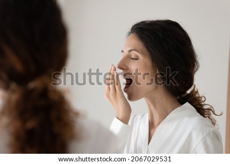 Close up young pretty woman wearing bathrobe reflected in mirror cover mouth with palm checking breath freshness after teeth cleaning. Teeth-care, dental care, clinic and mouthwash products ad concept 商業照片 © 