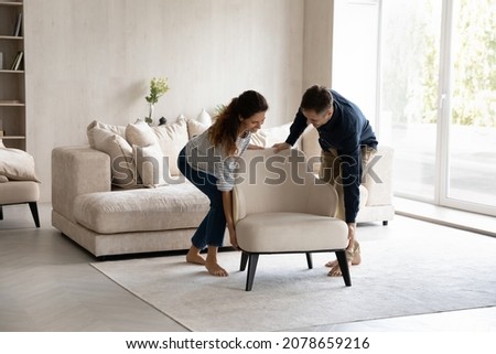 Spouses carrying modern armchair, placing furniture relocating into new home. Happy homeowners 35s couple enjoy moving day, start new life at own house. Fashionable apartment owners, bank loan concept Foto stock © 