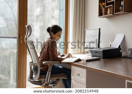 Concentrated young indian ethnicity woman sitting in comfortable adjustable ergonomic armchair with lumbar support, studying or working on computer in modern home office. distant workday concept. Foto stock © 