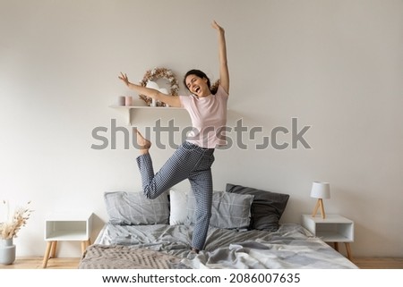 Overjoyed funny woman jumping on comfortable cozy bed at home, enjoying morning, starting new day, excited happy young female wearing pajama dancing to favorite music, having fun in modern bedroom Stock foto © 