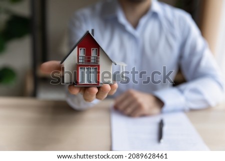 Close up realtor sit at table holds tiny house model, layout of cottage. Real estate purchase, new property, ownership, construction company make special offer to client, affordable dwelling concept Stockfoto © 