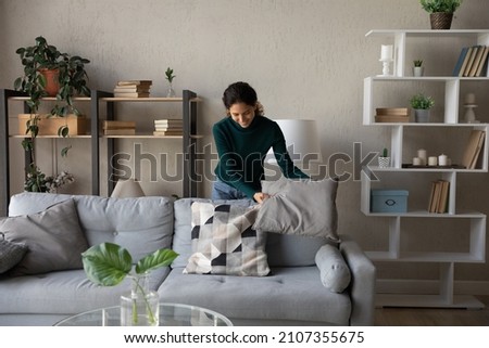 Happy millennial generation positive beautiful young housewife cleaning apartment, arranging stuff in cozy modern living room, put things on right places, feeling satisfied with comfort tidy house. ストックフォト © 