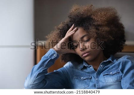 Frustrated unhappy African teen girl suffering from depression, melancholy at home, sitting on couch, touching head, feeling bad due to stress, hurt, despair, emotional problems, youth crisis Stock foto © 