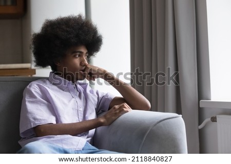 Thoughtful sad teen Black guy with retro Afro hairstyle sitting on sofa at home, looking away, thinking, feeling anxious, bored, concerned, suffering from depression. Youth problems concept Stock foto © 