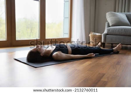 Young woman lying on mat listens meditative music through earbuds practicing asanas at home, do Corpse Savasana Dead Body, relaxing after yoga training. Repose, boost inner balance, no stress concept Photo stock © 