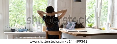 Panoramic image rear view female analyst worker sit at desk with hands behind head rest after productive work on laptop, looks out window. No stress, success, results, take break at workplace concept 商業照片 © 