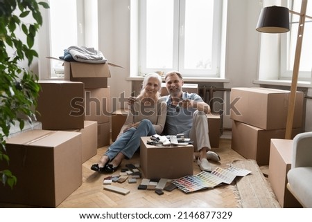 Happy spouses sit on floor near boxes with belongings smile showing keys from new house. Redecoration or repair works of dwelling, homeowners portrait, bank loan for older citizen, remodelling concept Imagine de stoc © 